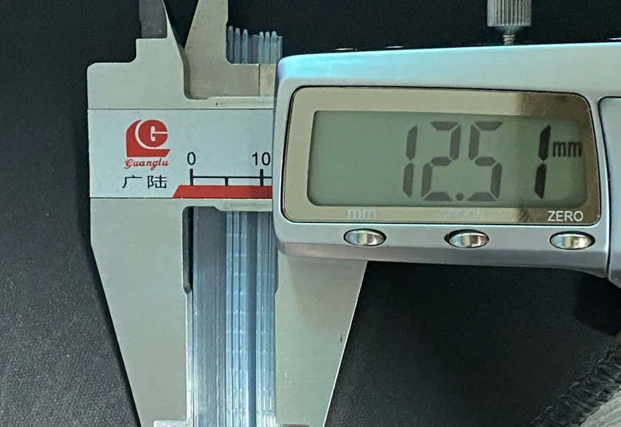 A digital caliper closed across a stack of clear zipper profile, its display reading 12.51 mm.